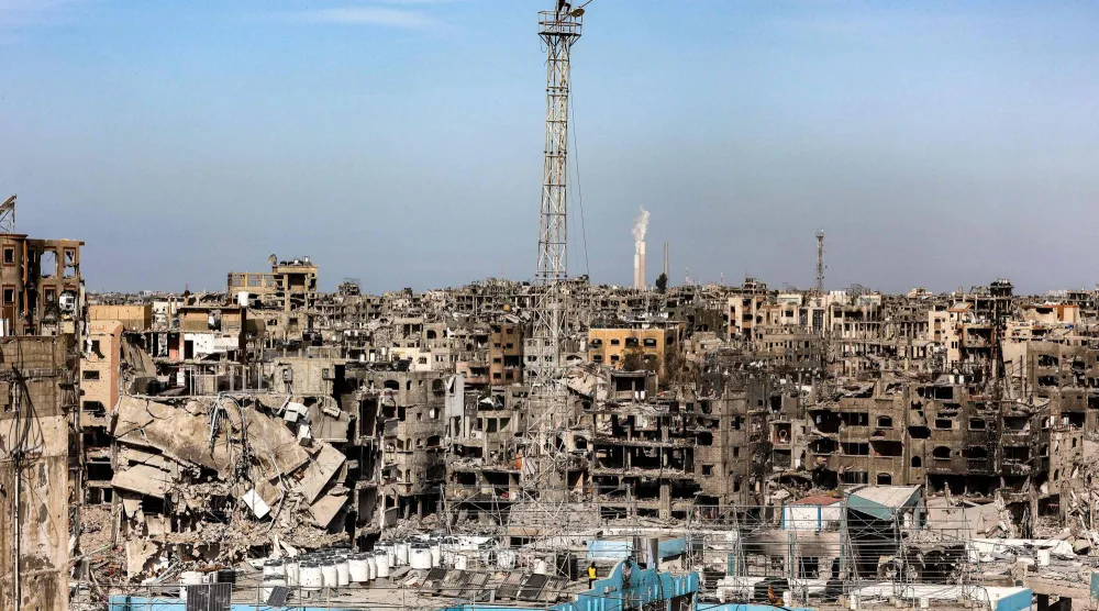 رجل يعلق علماً فلسطينياً على هوائي في مبنى شبه مدمّر كان يضم عيادة لـ«الأونروا» في مخيم جباليا بغزة (أ.ف.ب)