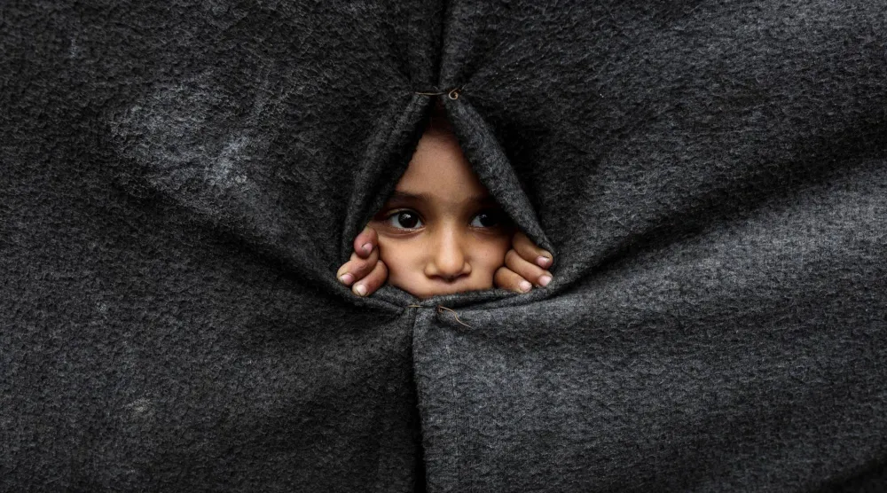 طفل فلسطيني نازح ينظر من خلال غطاء مصنوع من البطانيات أثناء لجوئه إلى مدرسة تديرها «الأونروا» في خان يونس جنوب قطاع غزة (رويترز)