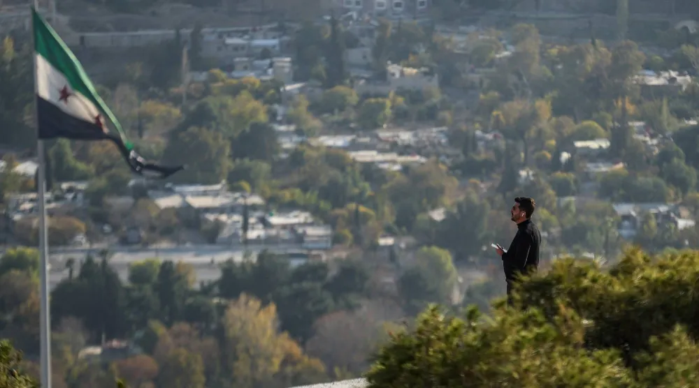 رجل يقف قرب علم سوري في نقطة مراقبة مرتفعة تطل على دمشق (د.ب.أ)