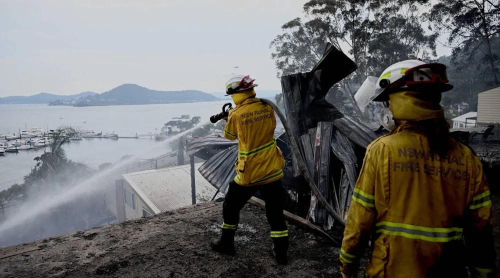 أحد أفراد خدمة إطفاء الحرائق الريفية في نيو ساوث ويلز يحمل خرطوم مياه بعد أن دمر حريق غابات منازلَ على طول طريق جلينروك في كوليونغ (أ.ب)