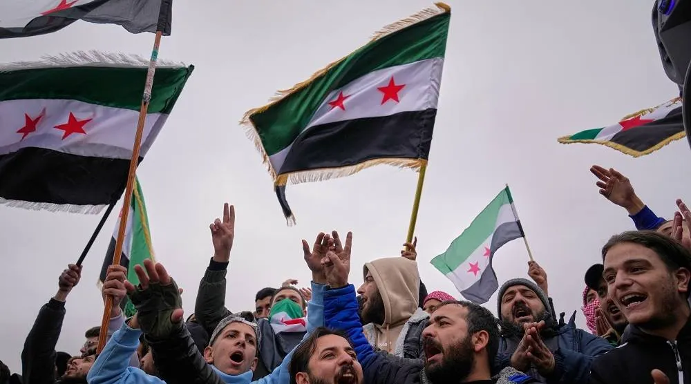 People celebrate and wave Syrian flags as they wait for a parade by the new Syrian army marking the first anniversary of the ousting of the Bashar al-Assad regime in Damascus, Syria, Monday, Dec. 8, 2025. (AP)