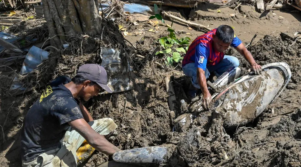 أشخاص يزيلون الطين من دراجة نارية إثر فيضانات مفاجئة في ميوريدو بمقاطعة بيدي جايا - إقليم آتشيه الإندونيسي (أ.ف.ب)