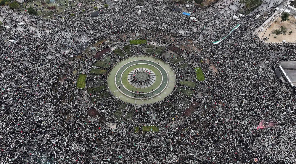 سوريون يحتشدون في ساحة الأمويين بدمشق بمناسبة ذكرى سقوط نظام بشار الأسد أمس (أ.ب) ... وفي الإطار الرئيس الشرع يحيّي الحشد  (أ.ب) 