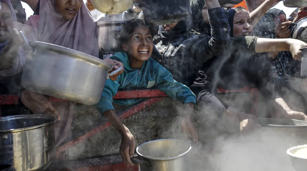 فلسطينيون نازحون داخلياً بينهم أطفال يحملون أواني الطعام في أثناء تجمعهم لتلقي الطعام من مطبخ خيري في مدينة غزة أغسطس الماضي (إ.ب.أ)