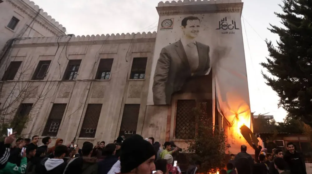 Hama residents set fire to a large banner of Bashar al Assad after armed factions seized the city last December (AFP)
