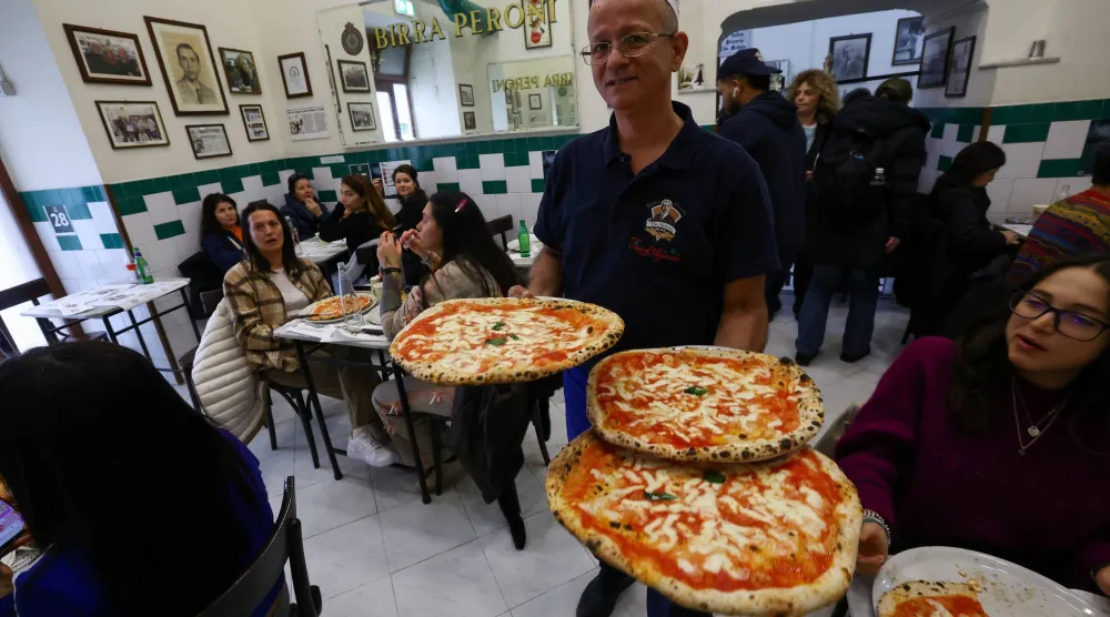 A waiter carries pizzas at L'antica Pizzeria da Michele as Italian cuisine awaits a crucial UNESCO decision that could recognize it as an Intangible Cultural Heritage of Humanity in Naples, Italy, December 5, 2025. (Reuters)