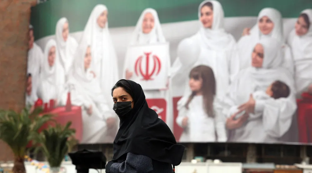 سيدة تمر أمام ملصق إعلاني عملاق على شكل علم إيران في ساحة ولي العصر بطهران اليوم الأربعاء (إ.ب.أ)