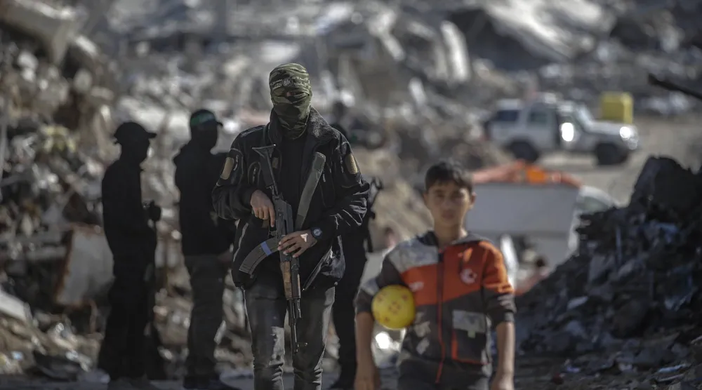 طفل فلسطيني يقف خلفه مقاتلون من «كتائب القسام» التابعة لـ«حماس» أثناء بحثهم عن جثث رهائن إسرائيليين في مخيم جباليا شمال غزة الاثنين (إ.ب.أ)