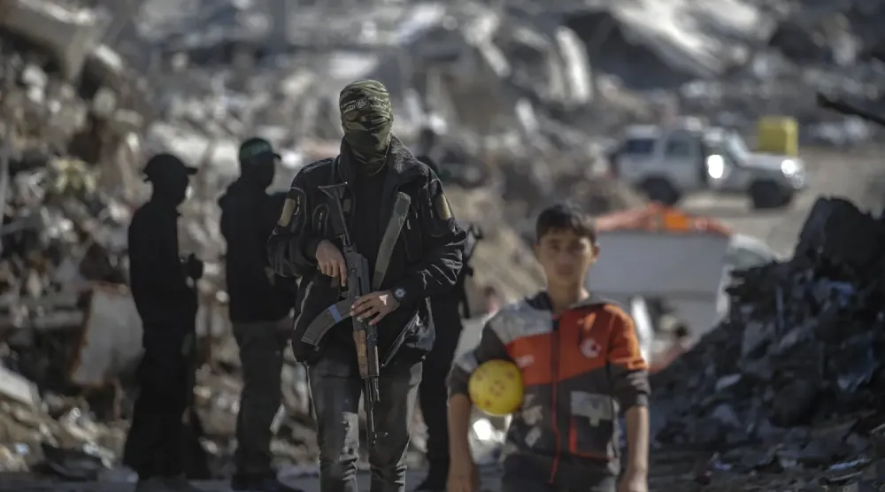 Gazze Şeridi'nin kuzeyindeki Cibaliye Mülteci Kampı’nda İsrailli rehinelerin cesetlerini arayan İzzeddin el-Kassam Tugayları savaşçılarının yanında duran Filistinli bir çocuk, 1 Aralık 2025 (EPA)