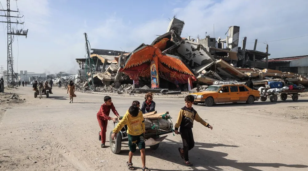 أطفال يجرون عربة أمام جدارية على مبنى مدمر في مخيم المغازي للاجئين خارج دير البلح (أ.ف.ب)