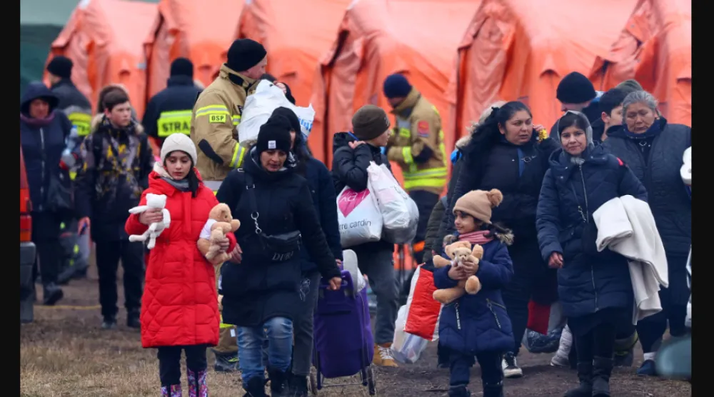 أشخاص يمرون بجوار الخيام في طريقهم للصعود إلى القطار بعد عبورهم الحدود من أوكرانيا إلى بولندا وسط الغزو الروسي (رويترز)