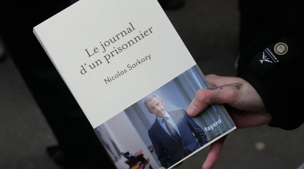 رجل يحمل كتاب «يوميات سجين» للرئيس الفرنسي السابق نيكولا ساركوزي أمام مكتبة في باريس الأربعاء 10 ديسمبر 2025 (أسوشييتد برس)