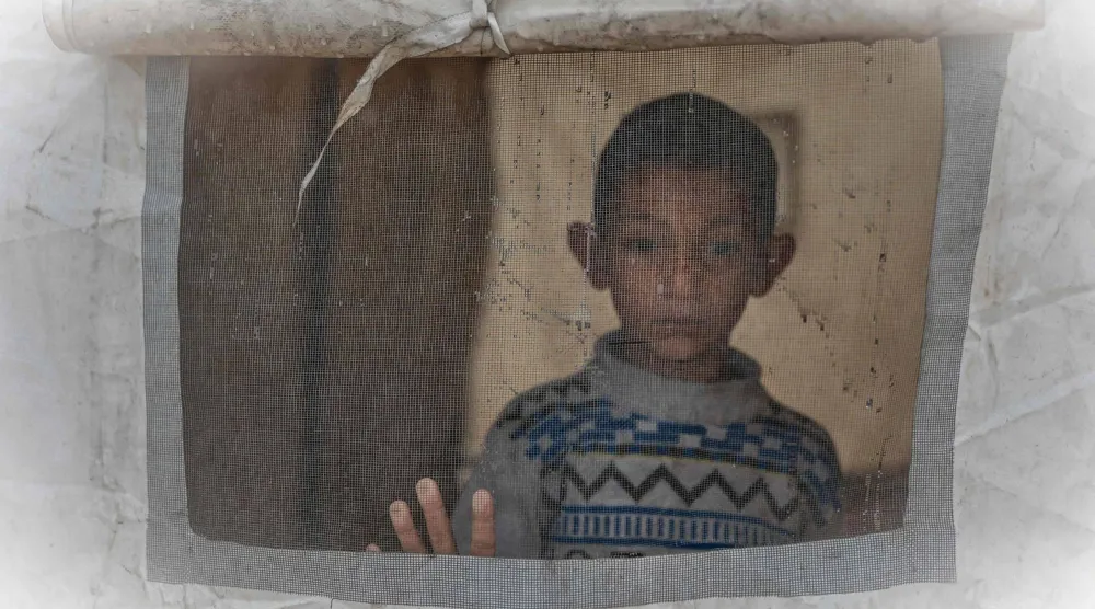 فتى فلسطيني ينظر من داخل خيمة في تجمع للنازحين يوم الخميس بحي الزيتون بمدينة غزة وسط موجة أمطار كثيفة تضرب القطاع (أ.ف.ب)