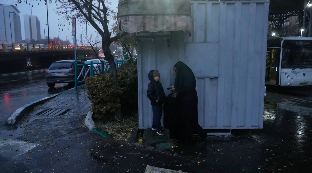 إيرانية تحتمي مع حفيدها من المطر في أحدر شوارع طهران الأربعاء (أ. ب)