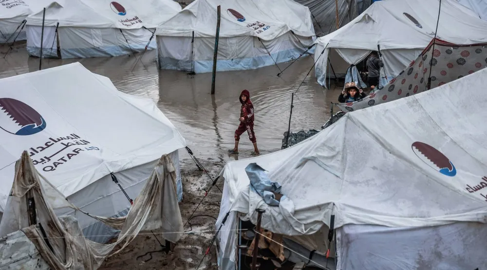 طفل يسير في زقاق غمرته المياه بمخيم مؤقت يؤوي نازحين فلسطينيين بعد هطول أمطار غزيرة في حي الزيتون الشهر الحالي (أ.ف.ب)