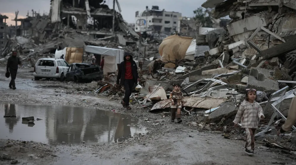 Palestinians walk through the rubble amid stormy weather in Gaza City Thursday, Dec. 11, 2025. (AP Photo/Jehad Alshrafi)
