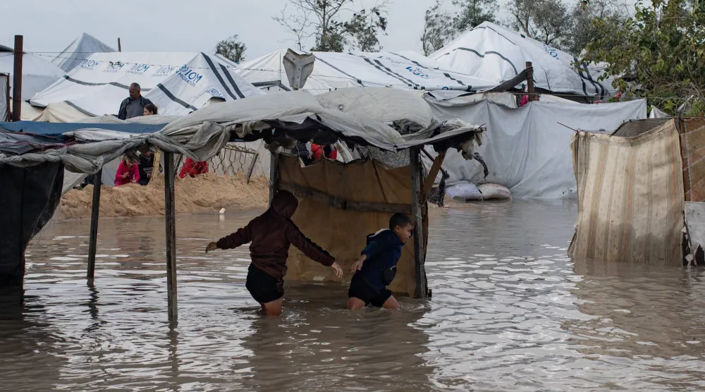 أطفال فلسطينيون يتحركون وسط مياه الأمطار التي أغرقت مخيمات الإيواء في خان يونس بجنوب قطاع غزة (إ.ب.أ)
