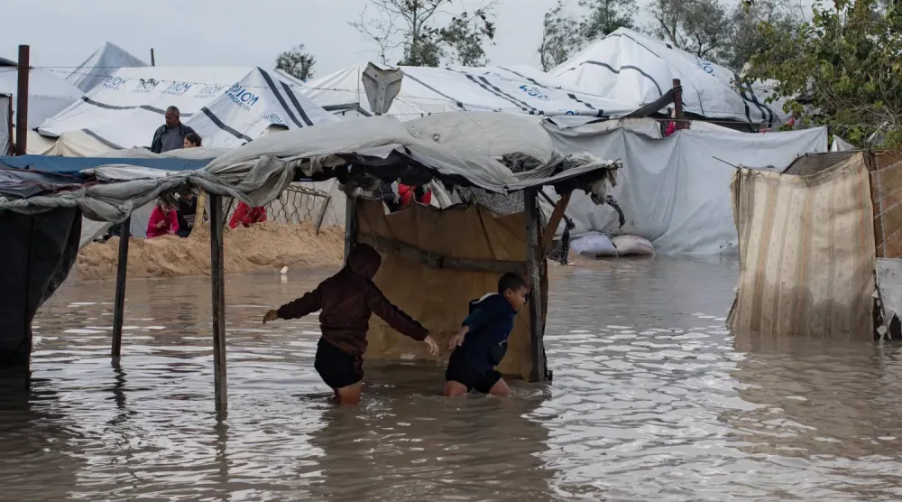 Filistinli çocuklar, Gazze Şeridi'nin güneyindeki Han Yunus'ta barınakları basan yağmur sularının içinden geçiyor (EPA)