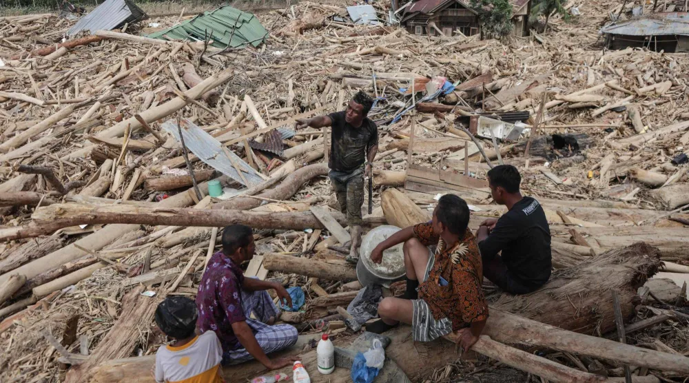 Residents rest as they search for the remains of their house, buried under piles of uprooted trees swept by the flash flood, in Lintang Baru village in Aceh Tamiang, northern Sumatra, on December 11, 2025. (Photo by Aditya Aji / AFP)