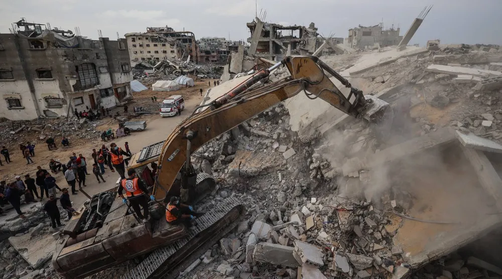 يستخدم أفراد الدفاع المدني حفارة للبحث عن رفات الضحايا في أنقاض مبنى مدمر في مخيم البريج للاجئين (أ.ف.ب)