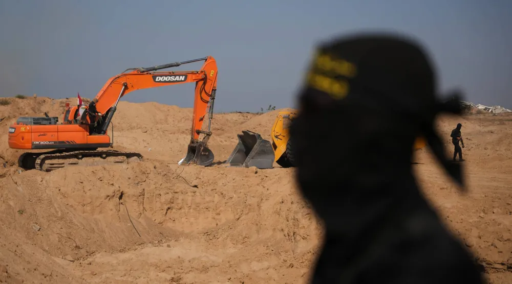 مقاتل من «الجهاد الإسلامي» يراقب عمالاً مصريين يحفرون بآلية ثقيلة بحثاً عن جثث المختطفين في النصيرات شمال قطاع غزة (أرشيفية - أ.ب)