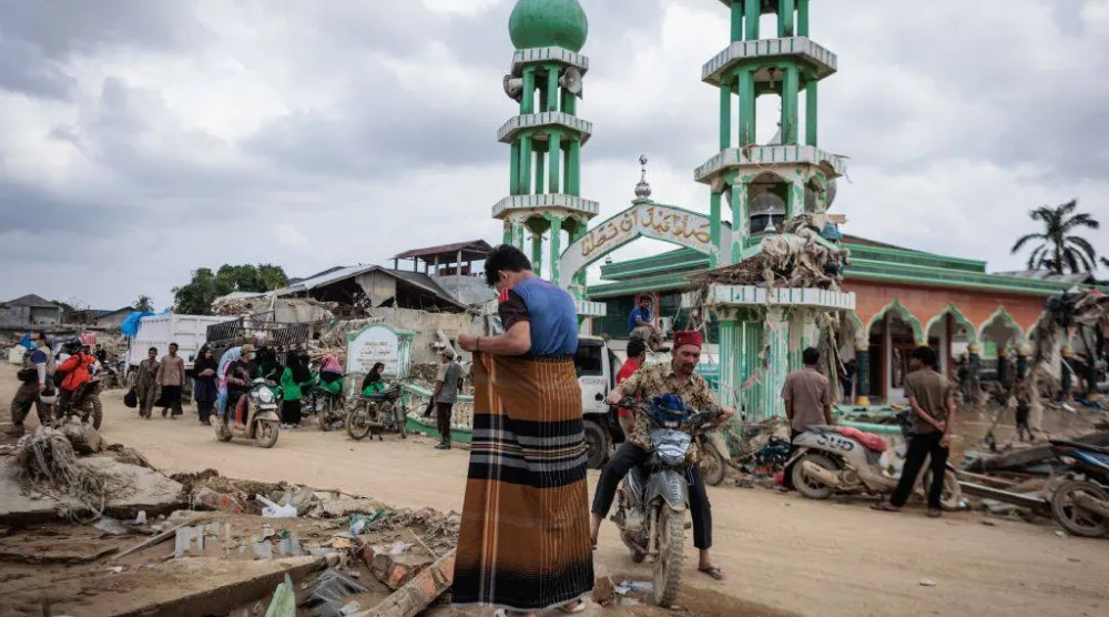 رجل يستعد لأداء صلاة الجمعة أمام مسجد الإحسان الذي دمرت الفيضانات جزءاً منه في آتشيه تاميانغ بإندونيسيا (أ.ف.ب)