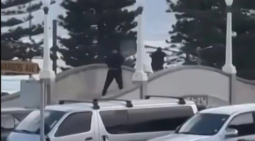 This screen grab made from UGC handout video footage courtesy of Timothy Brant-Coles shows two gunmen dressed in black firing multiple shots on a bridge at Bondi Beach in Sydney on December 14, 2025. (Photo by Handout / various sources / AFP)
