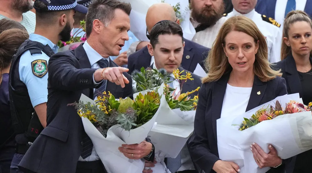 رئيس وزراء ولاية نيو ساوث ويلز كريس مينز (في الوسط) وكيلي سلون (على اليمين) زعيمة حزب المعارضة (الحزب الليبرالي) في نيو ساوث ويلز يستعدان لوضع أكاليل الزهور على نصب تذكاري لضحايا إطلاق النار خارج جناح بوندي في شاطئ بوندي بسيدني الاثنين 15 ديسمبر 2025 بعد يوم من وقوع الحادث (أ.ب)