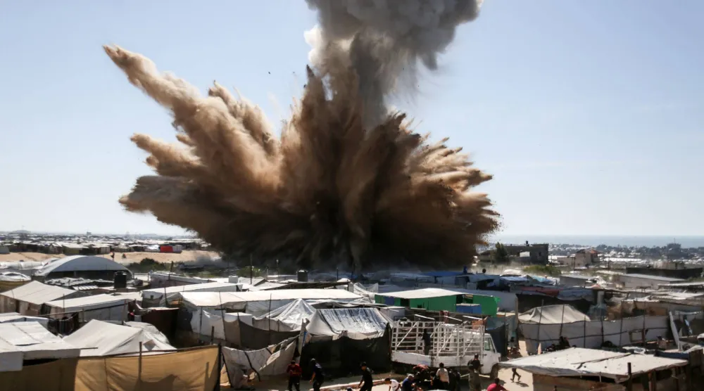 يركض الناس بحثاً عن مأوى بينما يتصاعد عمود من الدخان فوق الخيام في مخيم للنازحين الفلسطينيين شمال خان يونس (أ.ف.ب)