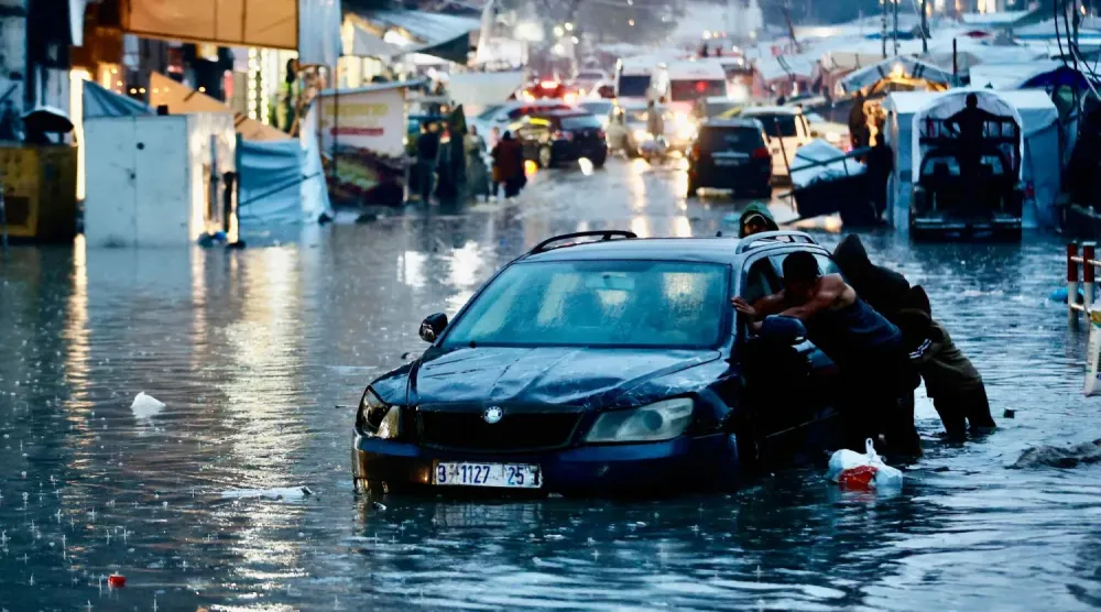 Şiddetli yağışlar nedeniyle meydana gelen sel sularının içinde kalmış bir arabayı iten yerlerinden edilmiş Filistinliler (AFP)