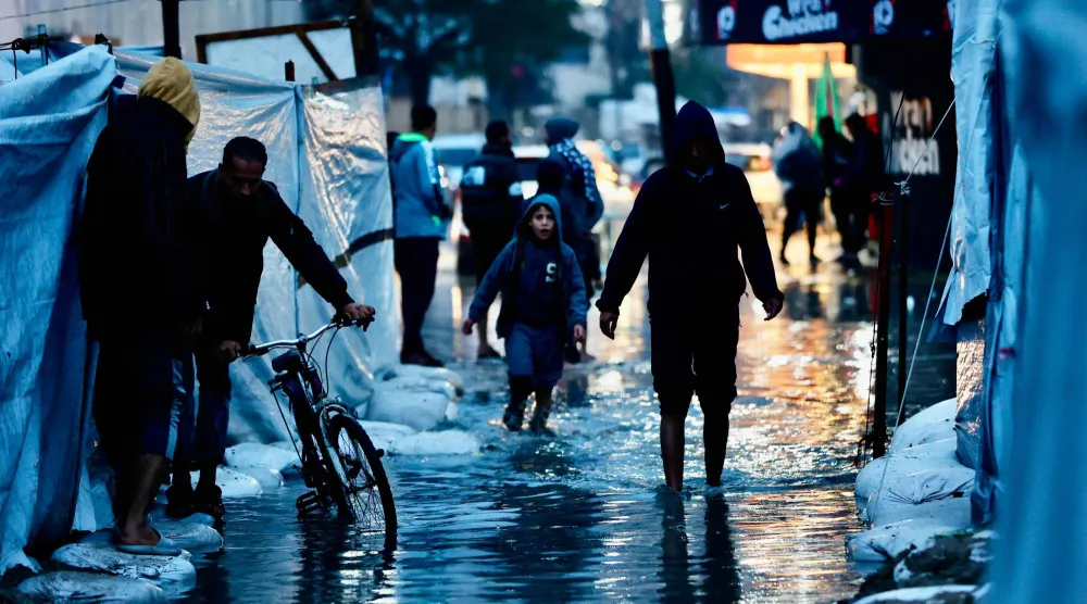 نازحون يمرون عبر برك المياه جراء الأمطار الغزيرة في مدينة غزة أمس (أ.ف.ب)