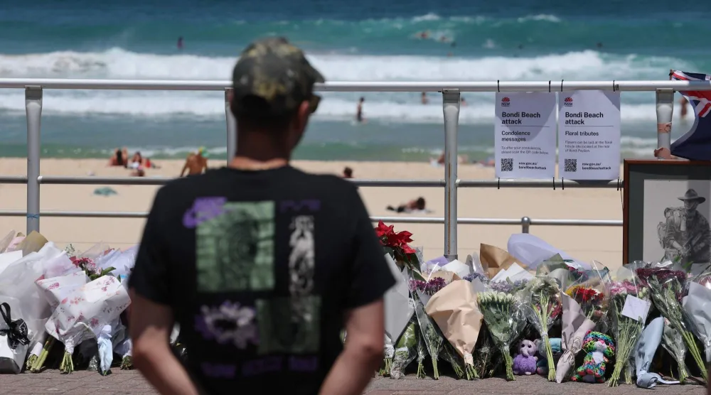 رجل ينظر إلى باقات الزهور التي وُضعت على ممشى شاطئ بونداي في سيدني حيث وقع الهجوم (أ.ف.ب)