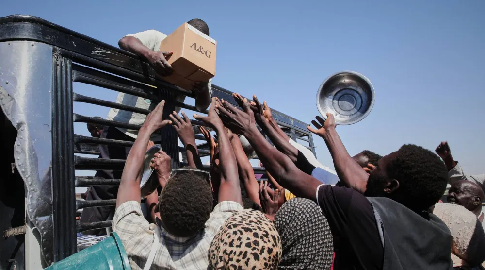 عائلات سودانية نازحة من الفاشر تتواصل مع عمال الإغاثة أثناء توزيعهم الإمدادات الغذائية بمخيم العفد الذي أُنشئ حديثاً في الضبعة بولاية شمال السودان (أ.ب)