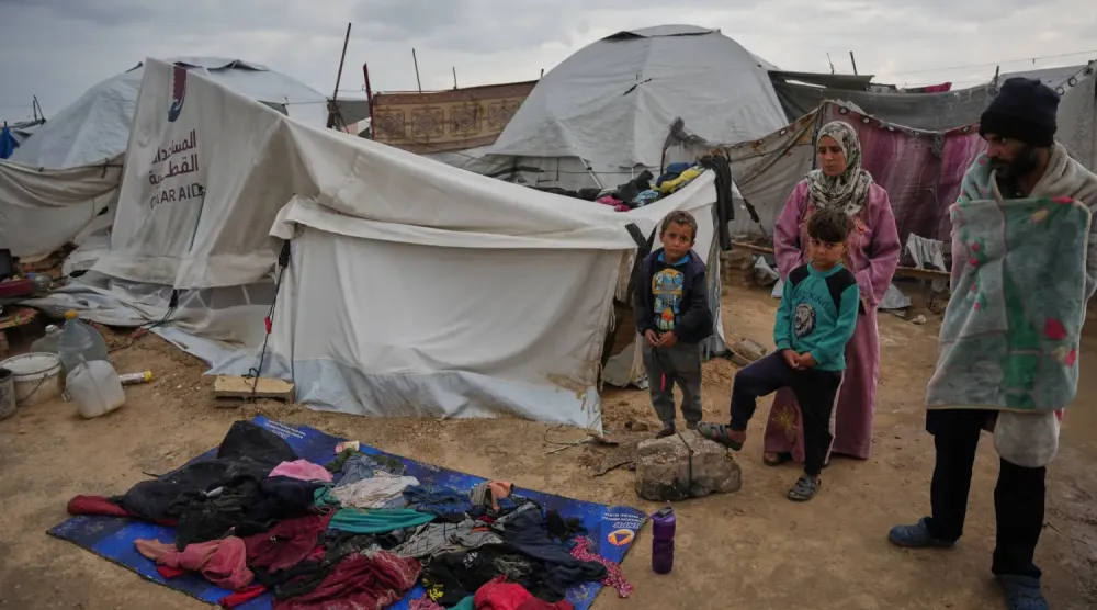 32 yaşındaki Rafet Alvan (sağda) ve ailesi, Gazze şehrinde soğuk bir sabah, sahilde kurulan geçici mülteci kampında çadırlarının önünde dururken, giysileri plastik bir örtü üzerinde kurumaya bırakılmış durumda. (AP)