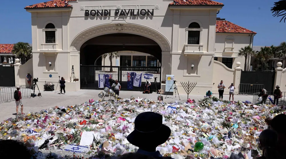 يقف المشيعون قرب أكوام من النصب التذكارية إحياءً لذكرى ضحايا حادثة إطلاق النار في شاطئ بونداي في سيدني (أ.ف.ب)