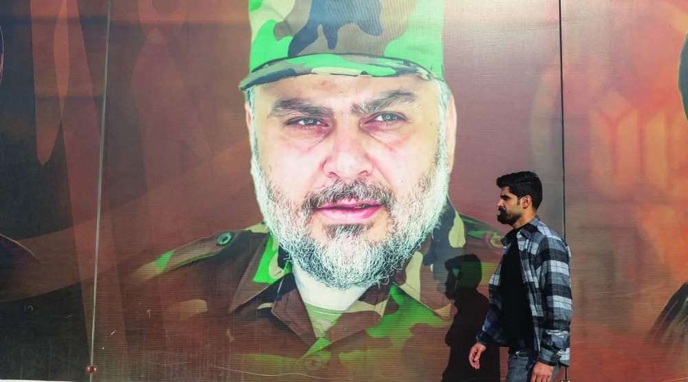 عراقي بأحد شوارع بغداد يمر أمام صورة لمقتدى الصدر مرتدياً الزي العسكري الخاص بـ«سرايا السلام»  (أ.ف.ب)