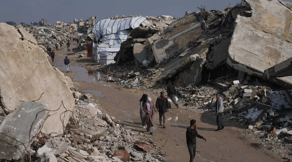 فلسطينيون يسيرون في شارع محاط بمبانٍ دُمّرت خلال العمليات الجوية والبرية الإسرائيلية في مدينة غزة، 17 ديسمبر 2025 (أ.ب)
