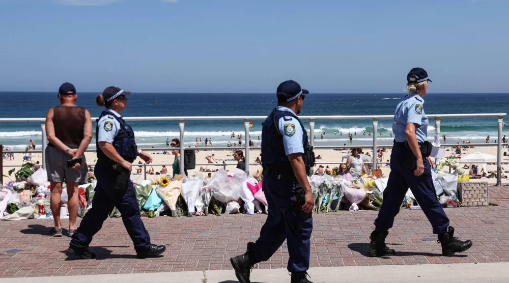 رجال شرطة يمرون أمام أكاليل زهور وُضعت على ممشى شاطئ بونداي في سيدني (أ.ف.ب)