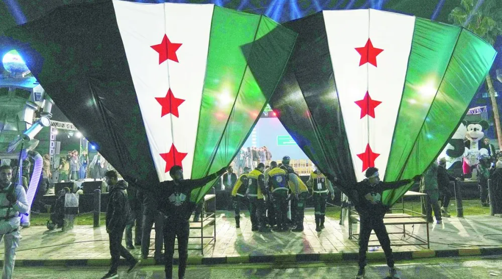 مواطنون سوريون يلوّحون بأعلامهم الوطنية خلال احتفالات الذكرى السنوية الأولى لإطاحة الرئيس السابق بشار الأسد في دمشق (أ.ب)