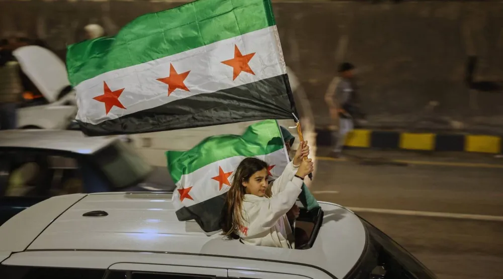 فتاة تحمل العلم السوري خلال الاحتفال بالذكرى السنوية الأولى للإطاحة بالنظام السابق في دمشق (أ.ب)