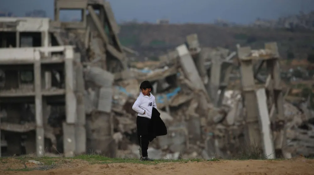 طفل فلسطيني يقف أمام منازل محطمة في مخيم النصيرات وسط قطاع غزة (أ.ف.ب)