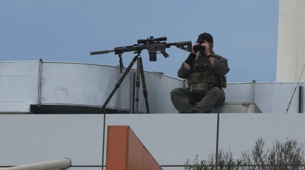 رجل ملثم من السلطات يجلس وبحوزته سلاح ناري على سطح مبنى في شاطئ بونداي في سيدني يوم الأحد 21 ديسمبر 2025 قبل مراسم إحياء ذكرى اليوم الوطني للتأمل لضحايا وناجين حادث إطلاق النار في بونداي في 14 ديسمبر (أ.ب)