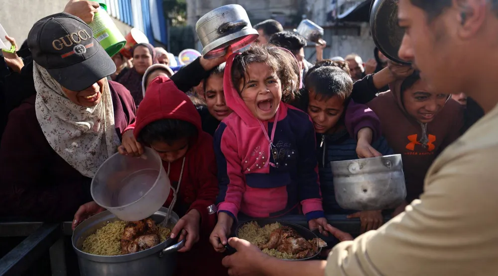 أطفال ينتظرون الحصول على نصيبهم من الطعام بمخيم النصيرات في غزة (أ.ف.ب)