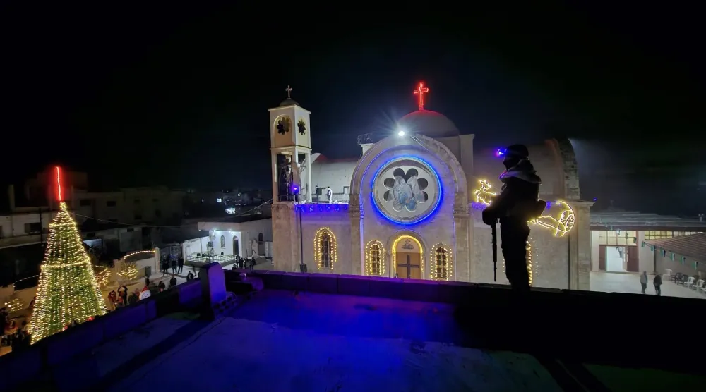 عنصر أمن سوري على سطح يطل على كنيسة القصير أثناء الاحتفال بإنارة شجرة الميلاد (متداولة)