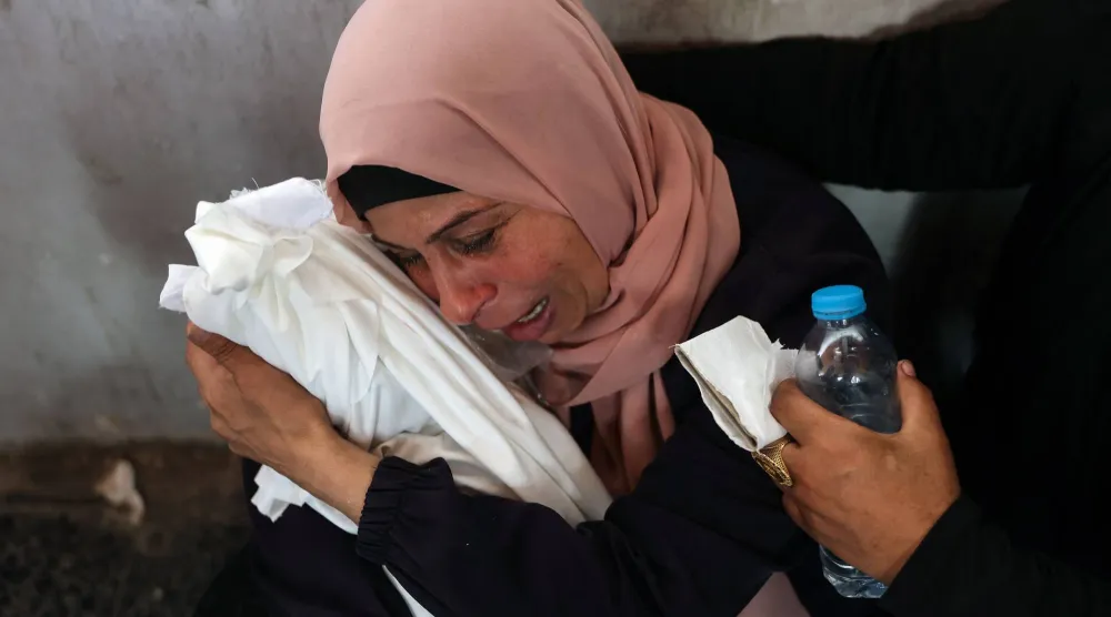 امرأة فلسطينية تبكي وهي تحمل طفلاً رضيعاً قُتل في غارة إسرائيلية بمدينة غزة (أ.ف.ب)