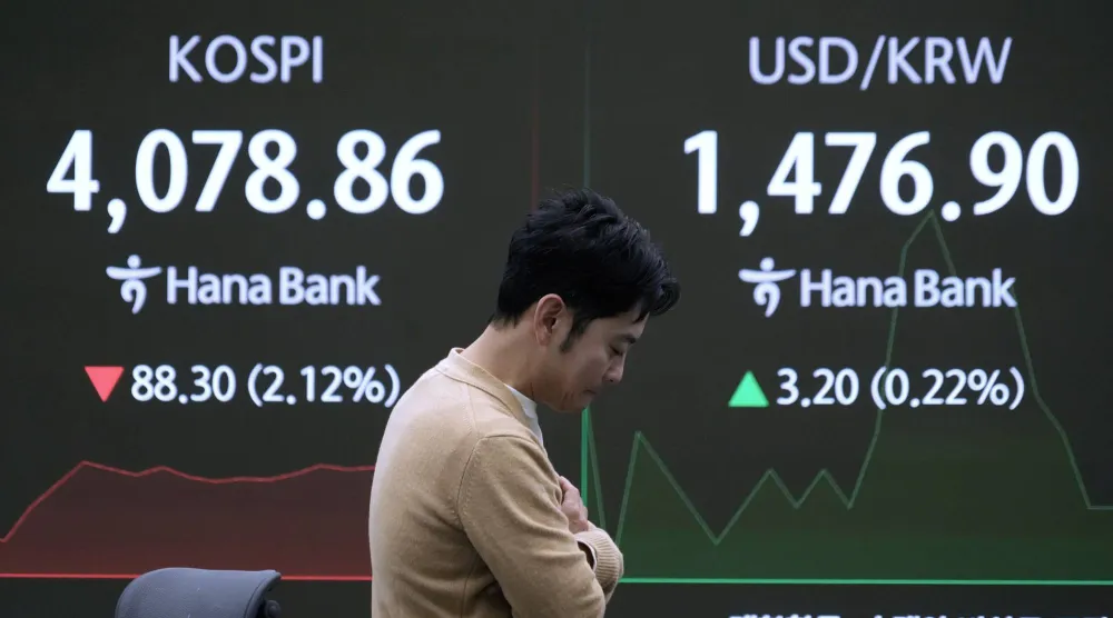 متداول عملات بجانب شاشة تعرض مؤشر «كوسبي» وسعر الدولار مقابل الوون في بنك هانا بسيول (أ.ب)