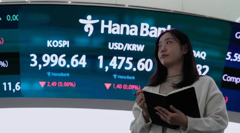 متداولة عملات بالقرب من شاشة تعرض مؤشر «كوسبي» وسعر صرف الدولار مقابل الوون في بنك هانا بسيول (أ.ب)