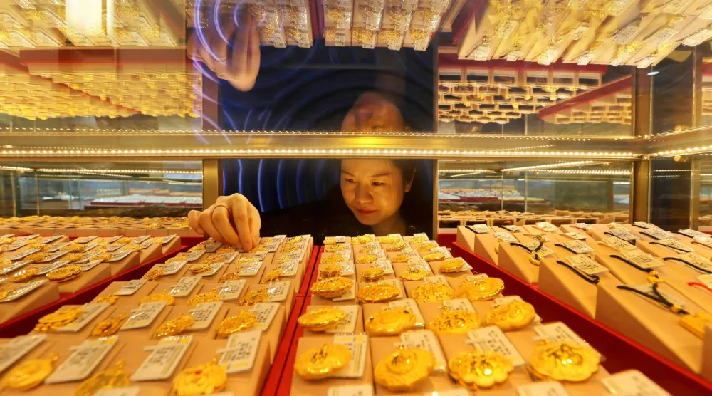 بائعة ترتب مجوهرات ذهبية معروضة للبيع في متجر بمدينة ليانيونغانغ بمقاطعة جيانغسو شرق الصين (أ.ف.ب)