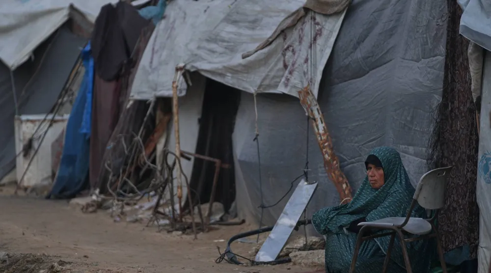 سيدة تجلس بجوار خيمتها داخل زقاق بمخيم مؤقت للنازحين الفلسطينيين في دير البلح وسط قطاع غزة (أ.ب)