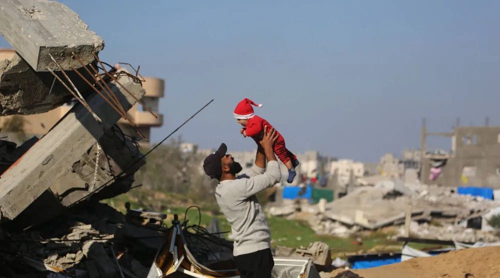 فلسطيني يحمل طفلاً بجوار أنقاض المباني المدمرة في مخيم جباليا للاجئين شمال قطاع غزة الأربعاء (أ.ف.ب)